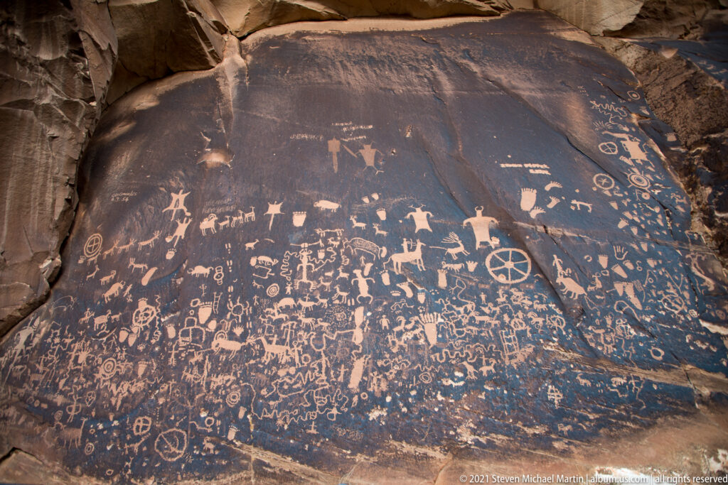 A broad dark sandstone panel is densely covered with pale petroglyphs of varied sizes and forms.