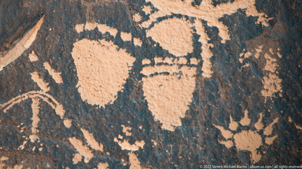 Two broad pale abstract forms fill a dark rock panel, with a curved line entering at lower left.