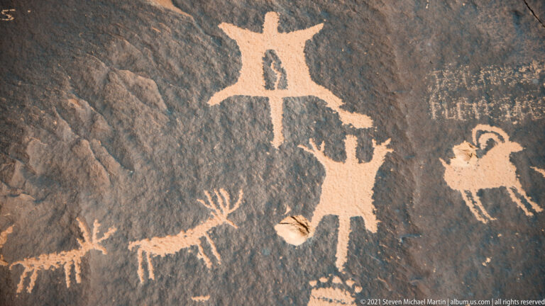 An arms-raised figure stands above several small quadrupeds carved across a dark rock surface.