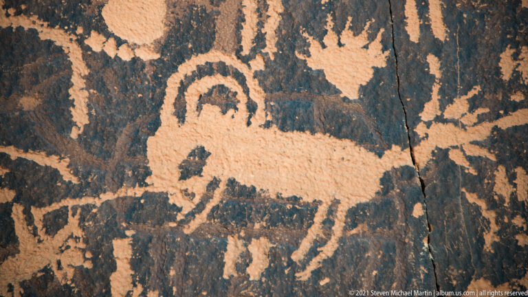 A large broad-bodied quadruped with branching head projections appears above smaller petroglyphs.