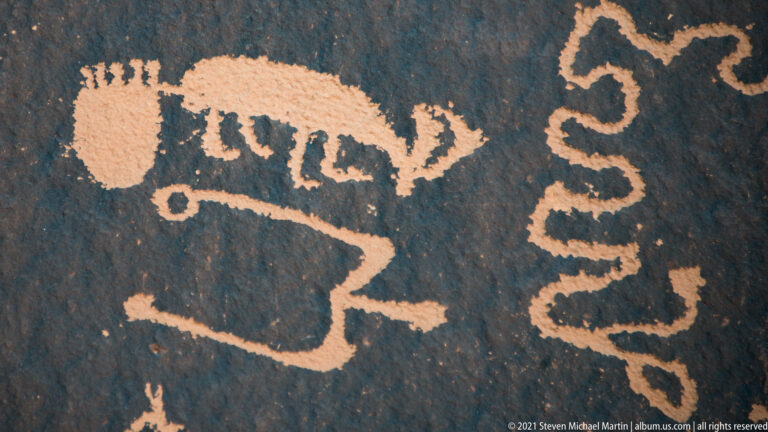 A pale quadruped sits above an angular outline and a winding line carved into dark stone.