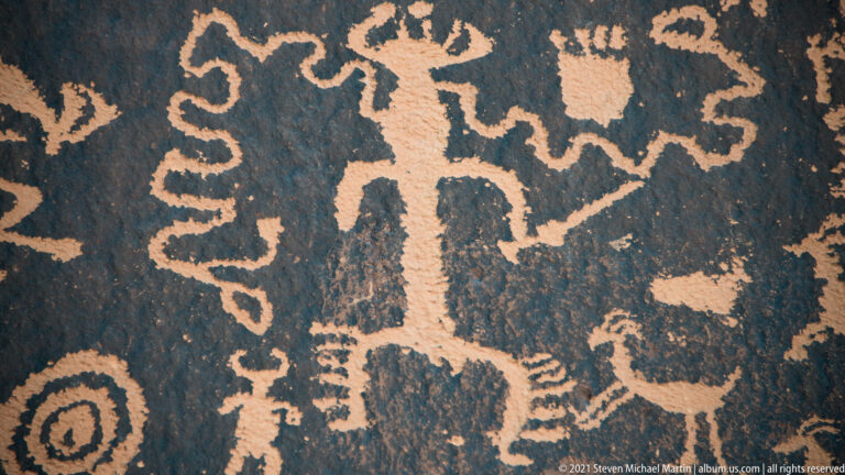 A tall upright figure stands amid animals, circles, and winding lines on a densely carved slab.