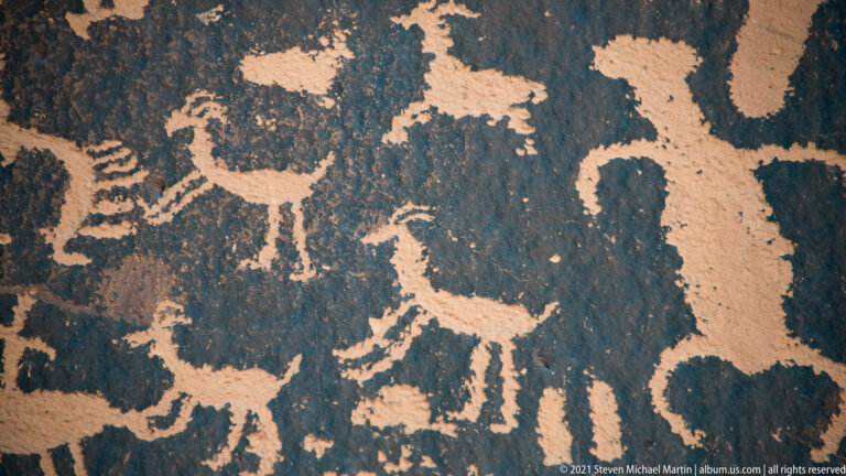 A large quadruped stands among smaller animal-like outlines, with an oval motif above on dark stone.