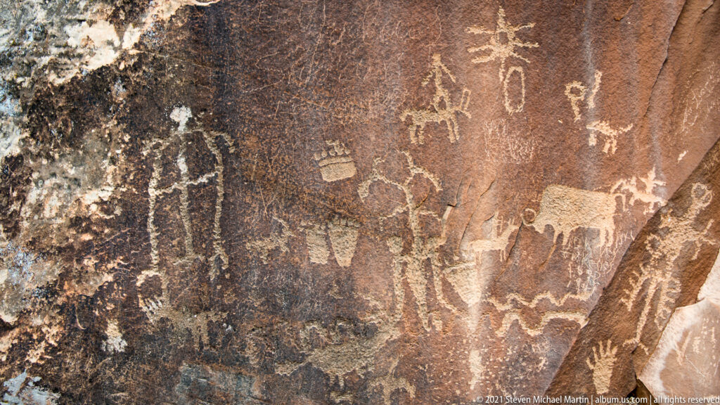 A close sandstone detail shows pale human-like figures, a hand-shaped mark, and small animal-like forms.
