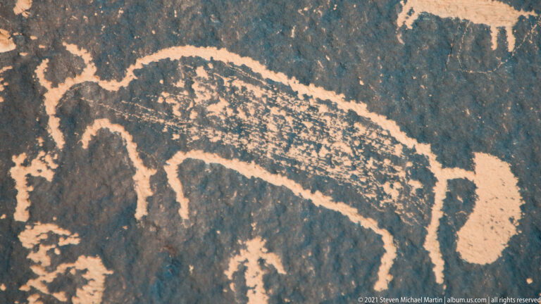 A long-backed quadruped in profile is outlined beside a separate vertical motif on dark stone.