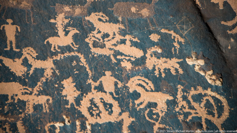 Animal-like outlines, upright figures, loops, and small marks densely cover a dark rock slab.