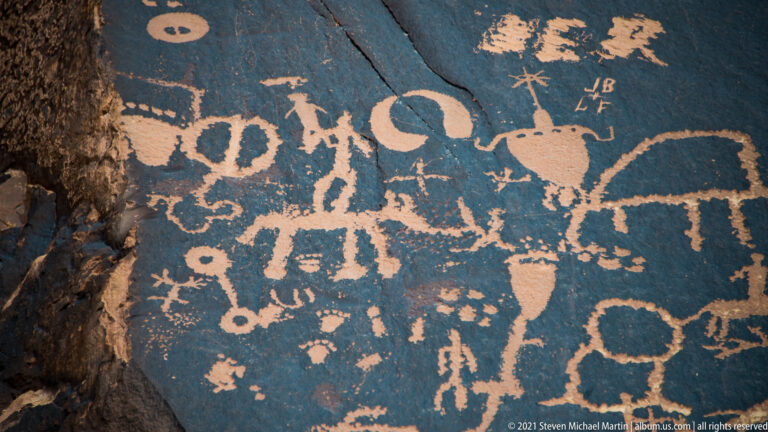 An angled rock panel holds animals, human-like figures, circles, and small letter-like marks near the top right.