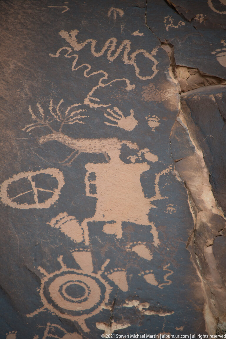 An extensive petroglyph field of circles, loops, and animal-like shapes follows a sloping slab beside a broken seam.
