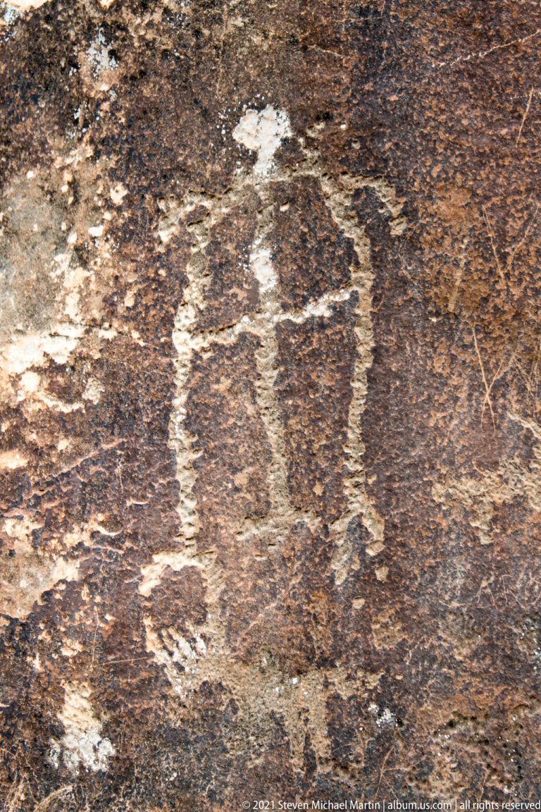 Faint pale petroglyph outlines appear against a mottled, rough sandstone surface in close view.