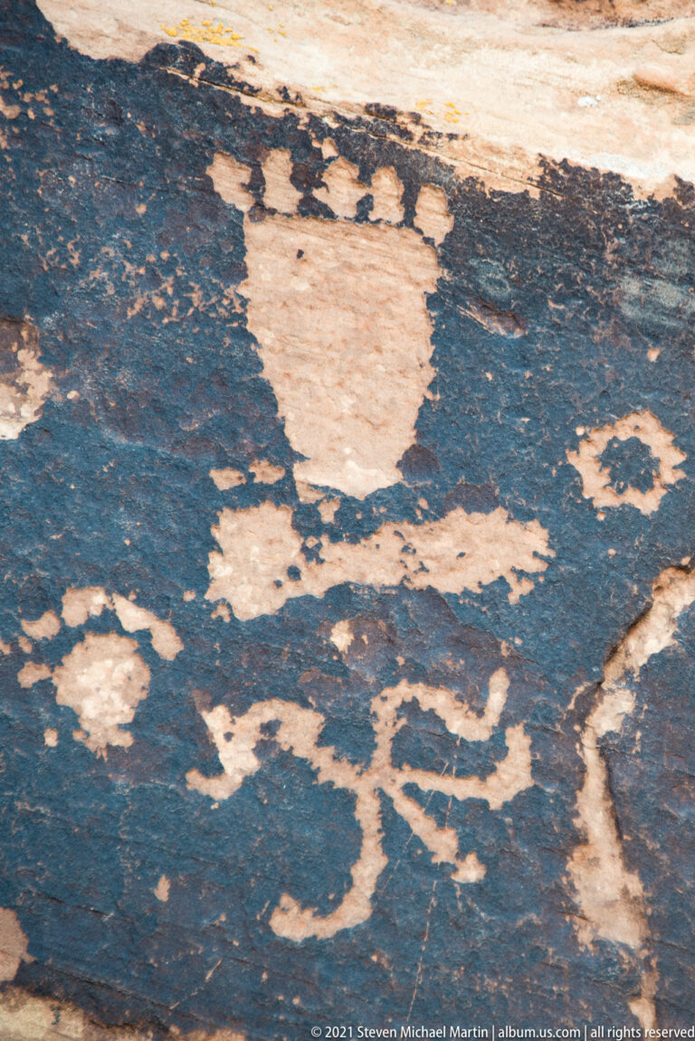 Pale pecked lines and shapes, including circles and angular forms, contrast with dark patina on a sandstone panel.