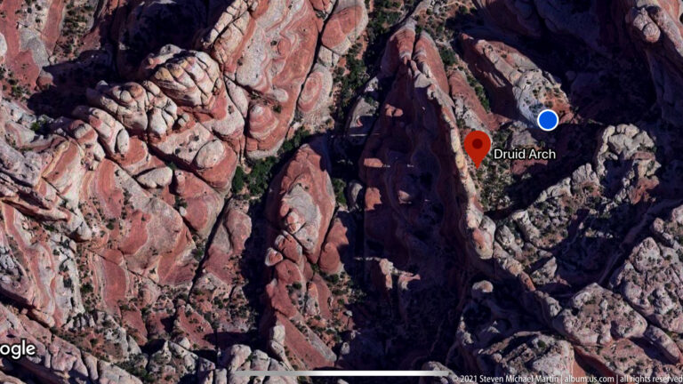 A satellite map marks Druid Arch with a red pin and blue dot amid rugged striped canyon terrain.