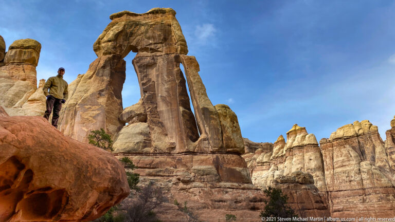 A hiker stands on a ledge beside the towering pillars and open span of Druid Arch.