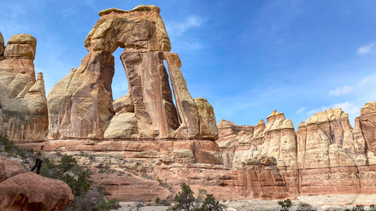 Druid Arch rises above a red boulder, with pale sandstone towers stretching across the basin to the right.