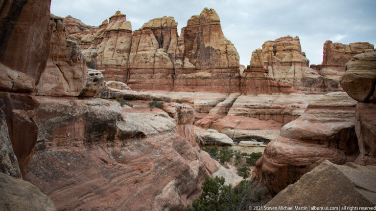 Banded sandstone walls and towers enclose a sandy canyon floor dotted with low junipers.