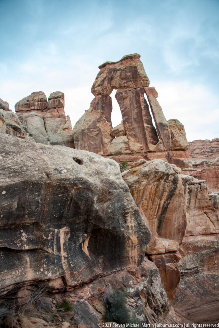 A dark slickrock shelf fills the foreground below Druid Arch, whose broad capstone spans tall sandstone supports.