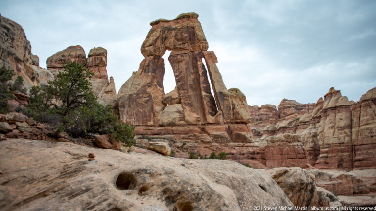 A dark pothole marks the pale foreground ledge, with Druid Arch rising beyond it among sandstone towers.