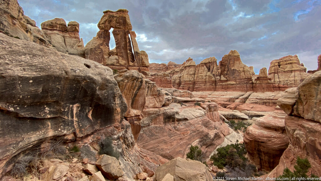 Druid Arch rises above red sandstone ledges and boulders, with layered spires extending across the canyon.