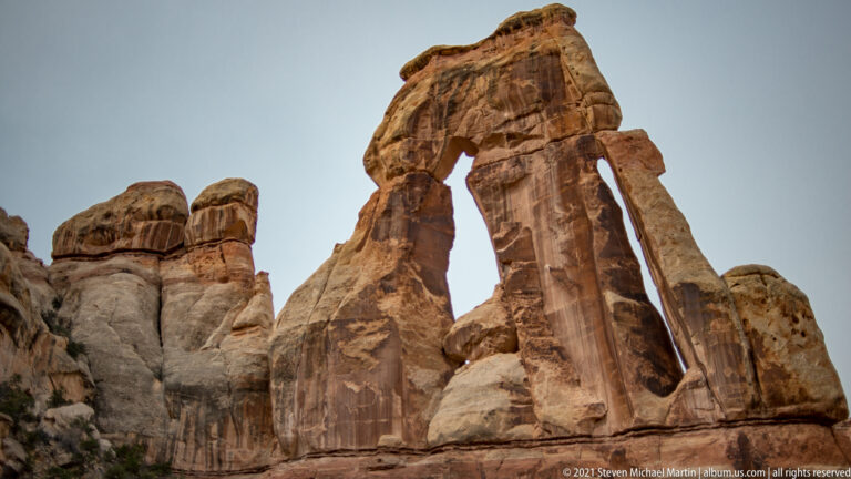 Druid Arch rises above two uneven sandstone supports, with rounded towers entering at left.