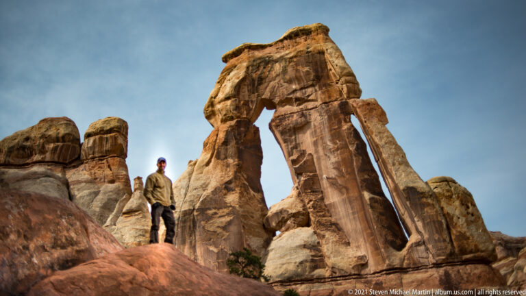 A visitor stands on a rock beneath Druid Arch’s capstone, with rounded towers to the left.