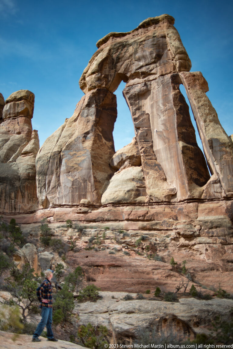 A small visitor walks across the lower left beneath Druid Arch’s broad sandstone span.