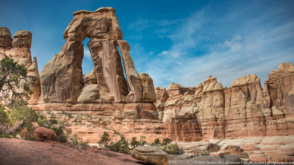 Druid Arch stands among sandstone towers and layered canyon walls beneath a broad blue sky.