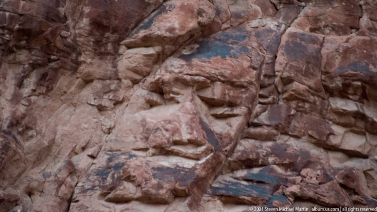 Close sandstone slabs show dark shallow pockets, narrow cracks, and uneven layered surfaces.