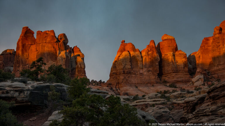 Tall sandstone towers glow orange around a central gap beneath a dim blue-gray sky.