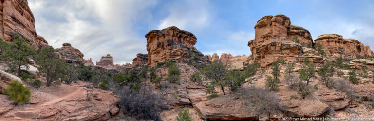 A pale rocky route winds below several sandstone towers, including a tall rounded pinnacle at right.