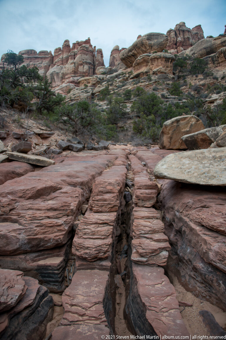 Parallel sandstone ridges run toward the viewer beside a narrow groove, with scrub and cliffs above.