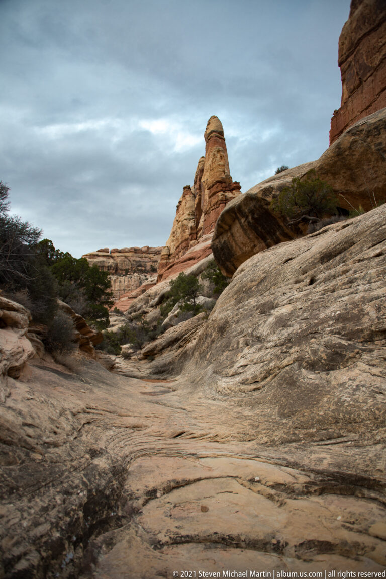 A smooth slickrock approach leads toward a rounded tower beneath a dark overhanging wall.