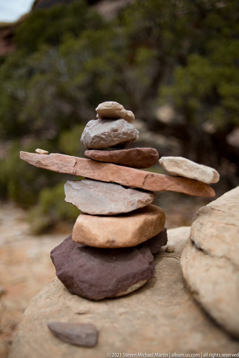 Broad tan, red, and gray stones form a balanced cairn against a softly blurred green-brown background.