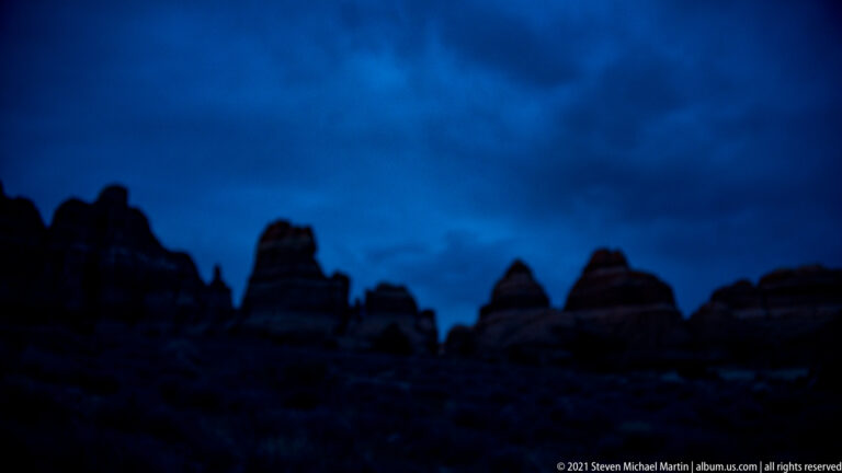 Dark sandstone pinnacles form a jagged skyline beneath a deep blue twilight sky.