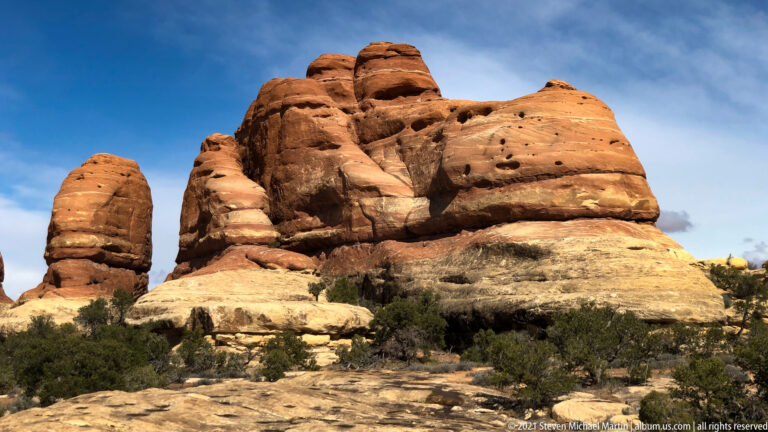 Close view of a rounded red sandstone formation with horizontal layers, ledges, and shallow hollows.