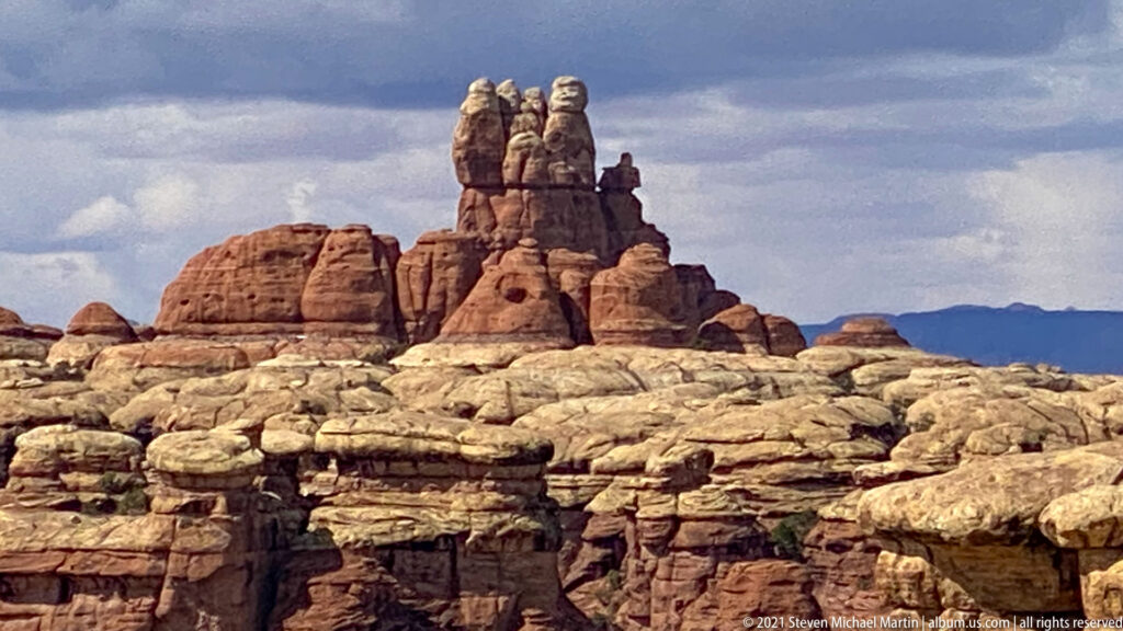 A dense skyline of sandstone towers stands behind pale layered canyon walls beneath a cloudy sky.