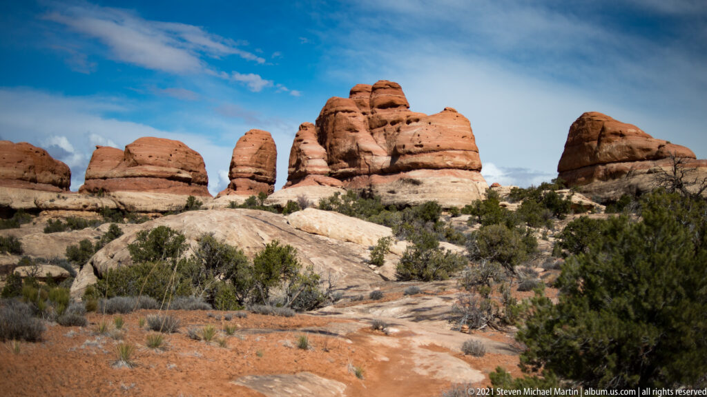 Rounded banded towers rise above a pale slickrock slope and scattered scrub.