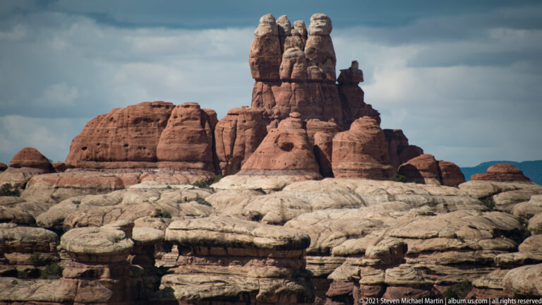 A cluster of narrow sandstone pinnacles rises above rounded red domes and pale foreground ledges.
