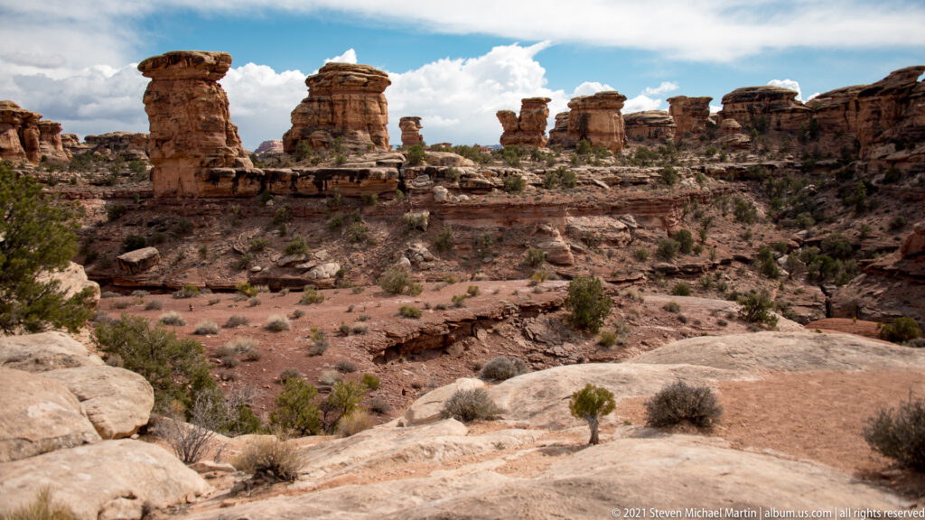 An elevated slickrock ledge overlooks a basin filled with sandstone spires and distant mesas.