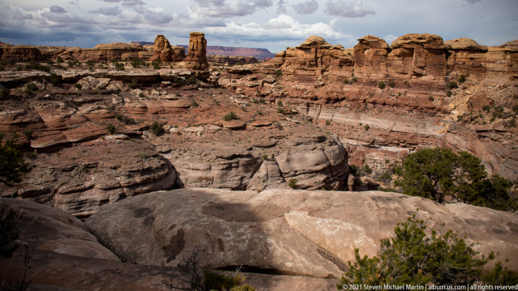 Pale slickrock overlooks a broad red basin enclosed by a ridge of rounded sandstone pinnacles.