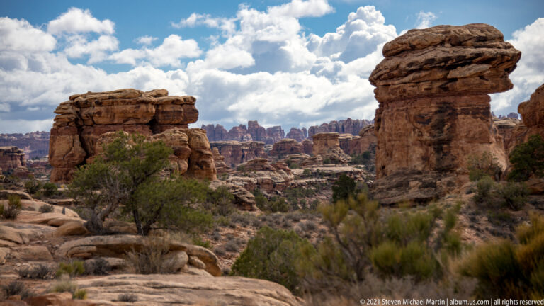 Large sandstone towers on both sides frame a deep basin of smaller pinnacles and shrubs.
