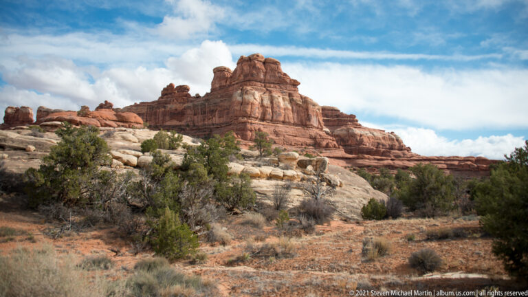 A broad red sandstone ridge with rounded towers rises above pale bedrock and dry grasses.