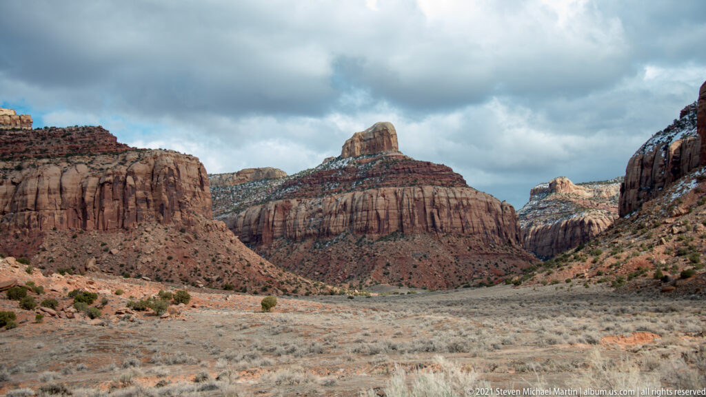 A rounded summit rises between steep sandstone cliffs with sparse vegetation and small snow patches.