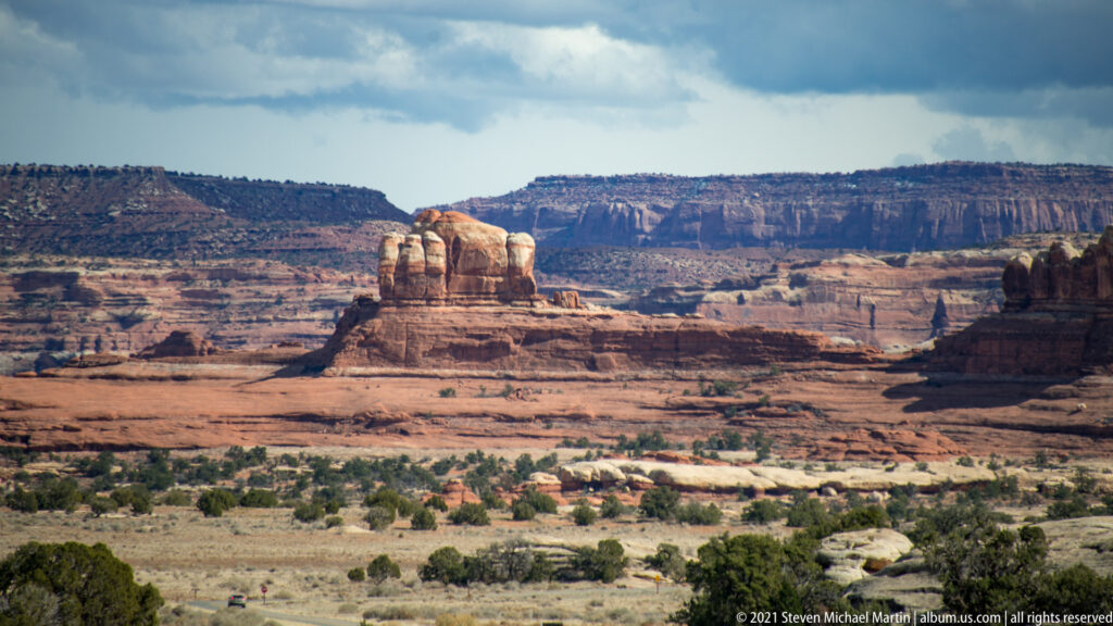 Rounded sandstone towers stand on a distant mesa above a broad basin with sparse shrubs.