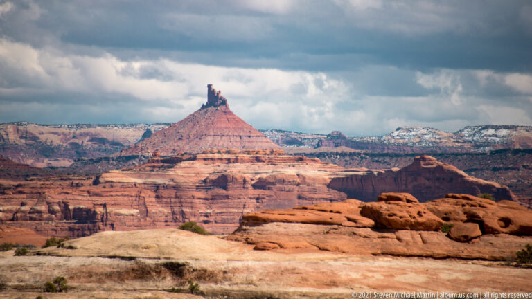 A pointed cluster of pinnacles crowns a conical red mesa above layered sandstone shelves.