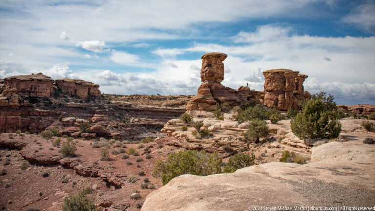 A broad caprock balances atop a narrow sandstone pedestal above a scrub-covered basin.