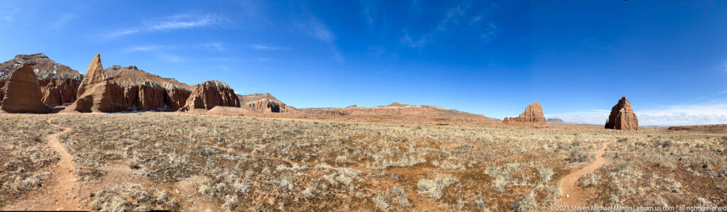 Narrow sandstone towers line the horizon beyond a winding path through dry grassland.