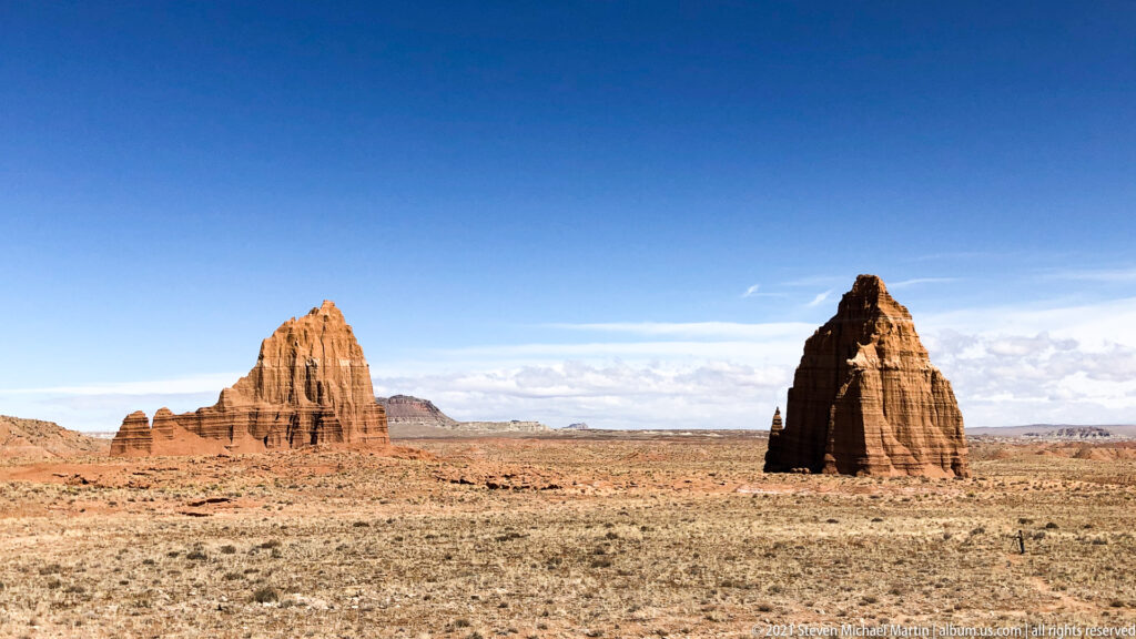 Two sandstone towers, one pale and broad and one dark and conical, rise from open grassland.