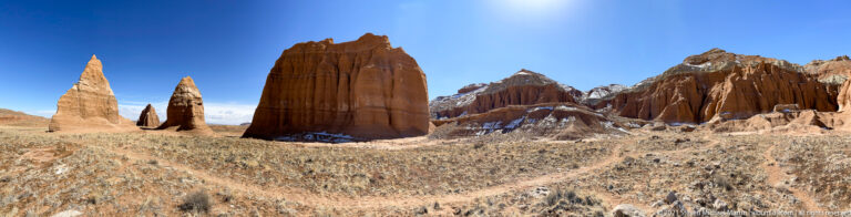 Tall red pinnacles rise from dry grassland, with small snow patches at several bases.