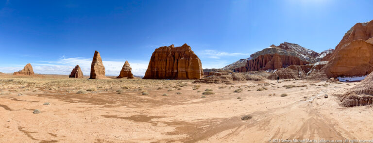 A grooved red sandstone monolith rises in front of snow-dusted ridges and dry grassland.