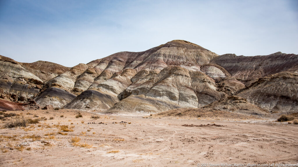 Pale striped slopes and a rounded summit lie before darker red-brown hills.