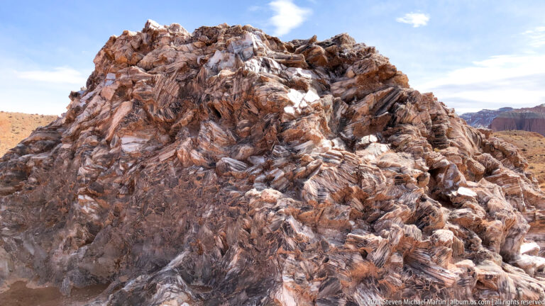 Jagged white, gray, mauve, and rust-colored rock fragments fill the foreground below a small patch of blue sky.